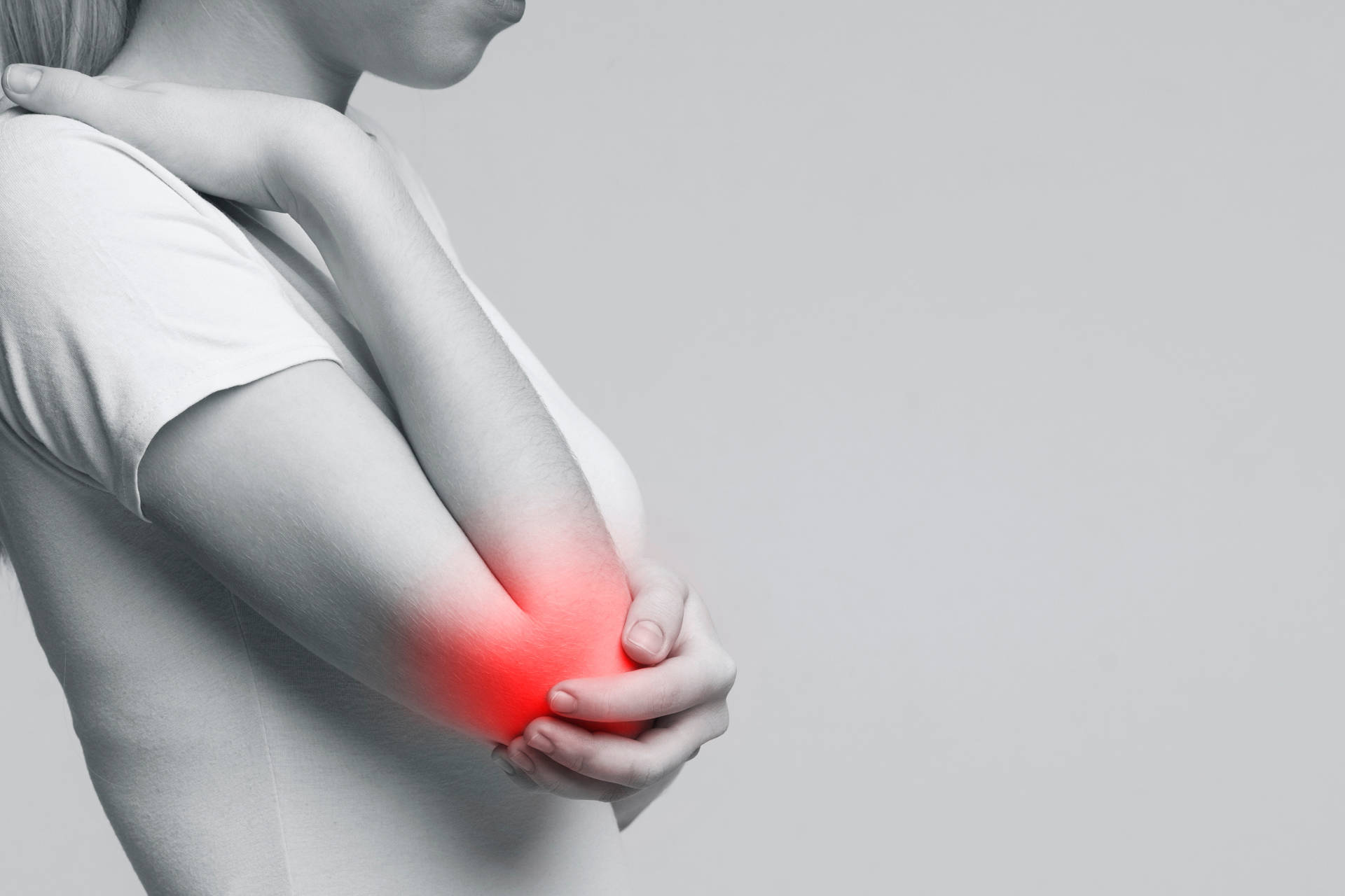 Eine Frau mit Ellenbogenschmerzen, z. B. Tennisellenbogen, fasst sich an den schmerzenden Ellenbogen.